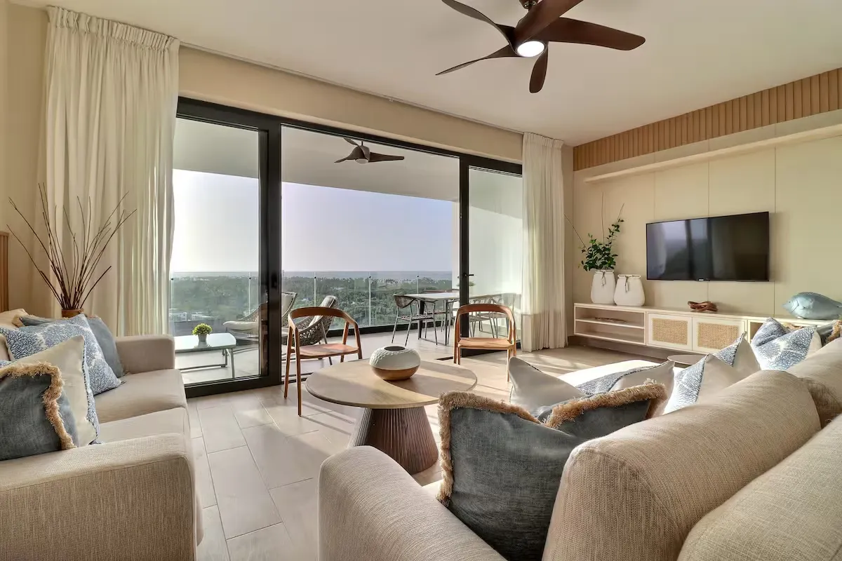 Sala de estar enmarcada por puertas del piso al techo que se abren hacia la terraza con vista al mar